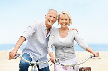 Obraz premium Portrait, bicycle and mature couple by ocean for bonding on vacation, holiday and summer weekend. Happy, embrace and man with woman on bike for travel, eco friendly transport and relax by seaside