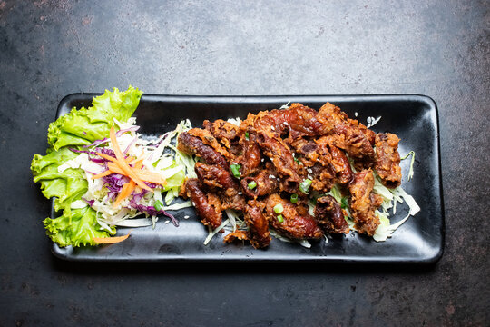 Deep fried pork intestines served with fresh side salad on a black rectangular plate over dark background.