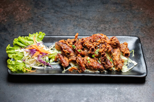 Deep fried pork intestines served with fresh side salad on a black rectangular plate over dark background.