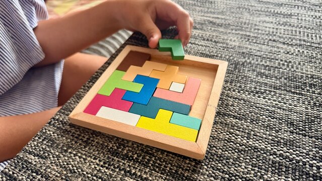 Child solving colorful wooden tangram puzzle on table. Educational toy for developing logical thinking and motor skills