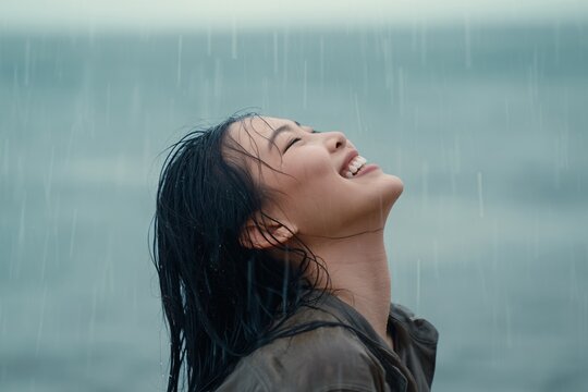 Happy woman enjoying the rain at the beach with her eyes shut and a big smile on her face