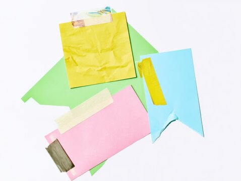 A photo of four overlapping paper notes of varied shapes (square, rectangle, arrow), colors (yellow, green, pink, blue), and textures (crumpled, smooth, torn), attached with different washi tapes