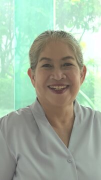 Happy smiling middle aged asian woman with positive friendly expression in urban environment, vertical video