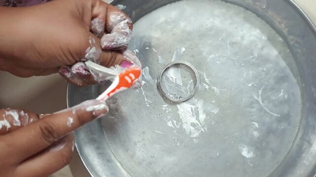 Woman cleaning dirty silver bangles with toothbrush and paste at home, close-up