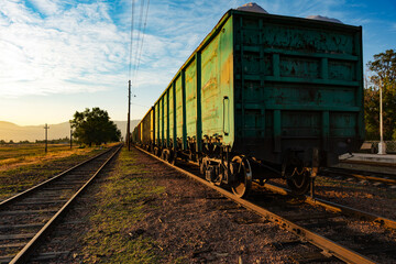A perspective shot of a long freight train with weathered green open-top gondola wagons standing on railway tracks. © Dina Luk
