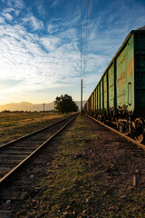 A perspective shot of a long freight train with weathered green open-top gondola wagons standing on railway tracks. © Dina Luk