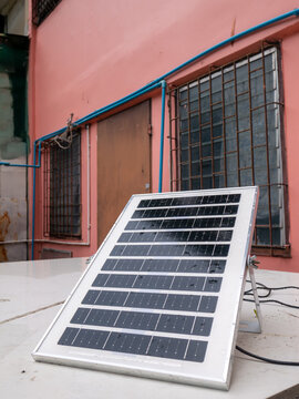 Small solar panel leaning against wall on rooftop with rain water droplets renewable energy DIY home installation outdoor