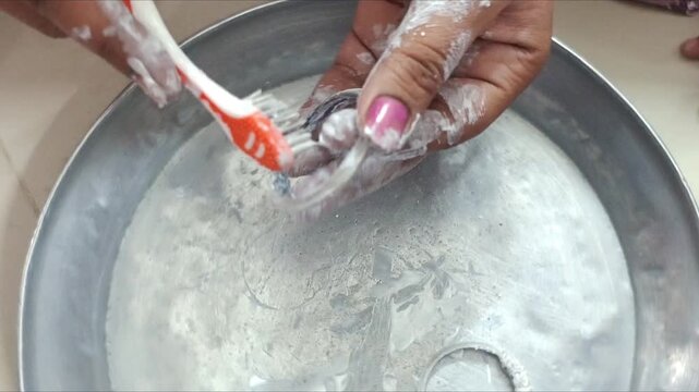 Woman cleaning dirty silver bangles with toothbrush and paste at home, close-up