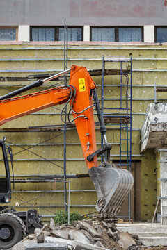 An excavator is moving dirt and rocks at a construction site. Workers are seen preparing the area for new buildings while scaffolding is present