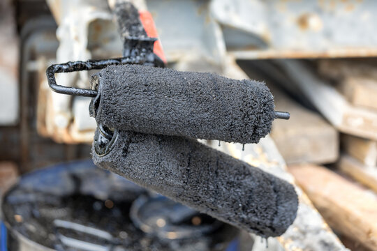 Workers use rollers covered in bitumen mastic for waterproofing a foundation at a construction site. The process helps protect against water damage