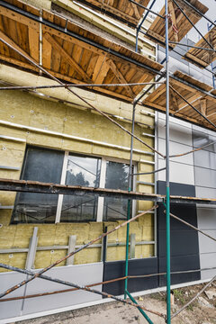 Workers install mineral wool insulation on the building's facade. Scaffolding is set up to allow safe access to higher areas. The work is ongoing at a construction site