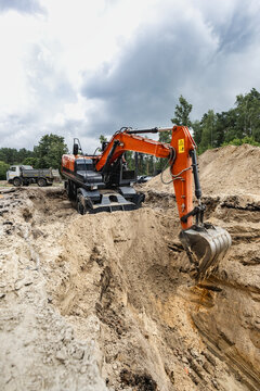 Excavator digs into the ground at a construction site. The machine is moving earth and creating a trench for building work. Trucks are visible nearby