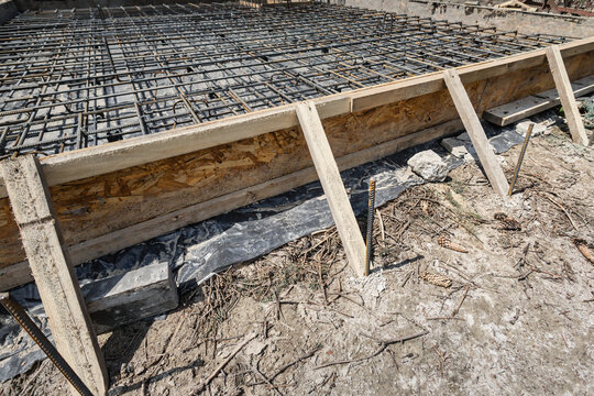 Workers place steel reinforcement bars into position for a concrete pour. The site is under construction with materials ready for the pour