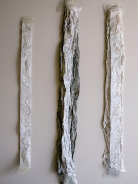 A photo of three long, narrow paper strips (like receipts) of varied lengths, arranged vertically, all heavily crumpled and attached with clear tape