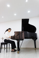 Portrait of a beautiful Hispanic woman playing a classical piano in the hall of a classical music conservatory in Neiva, Huila, Colombia. Concept of leisure activity © Ludaro