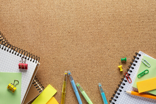 Notepads, pencil, sticky notes, paper sheets, paper clips and binder clips  on cork board  with copy space for text.  Top view of colorful school supplies.