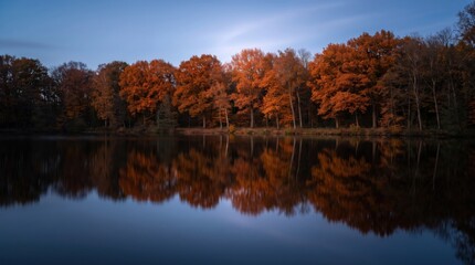 Obraz premium Autumn forest reflecting in a calm dark lake at golden hour with reflection