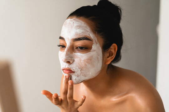A woman applying a face mask at home while looking in the mirror