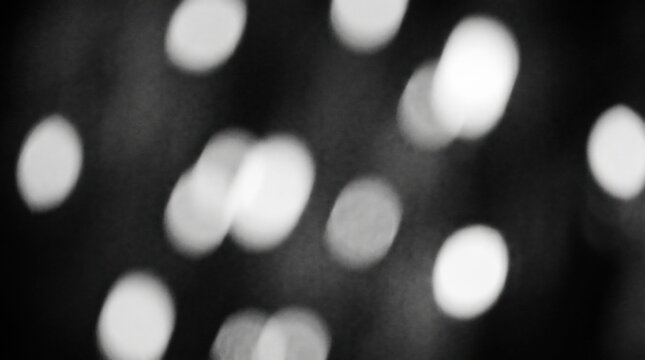 Monochromatic abstract background featuring soft glowing circular lights scattered across a deep dark void with grainy background with white composition blurred