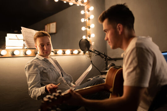 Male composer instructing guitarist in studio. Men in sound studio