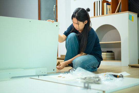 Young Asian Woman Assembling Flat Pack Furniture on Floor at Home