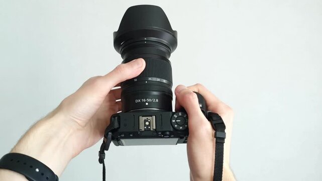 Human hand firmly holds professional camera with lens hood pointing forward on white background