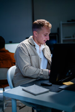 A focused blond cybersecurity analyst holds a pen while analysing on-screen data in a blue-lit cyber operations centre, under the blue glow of security dashboards.