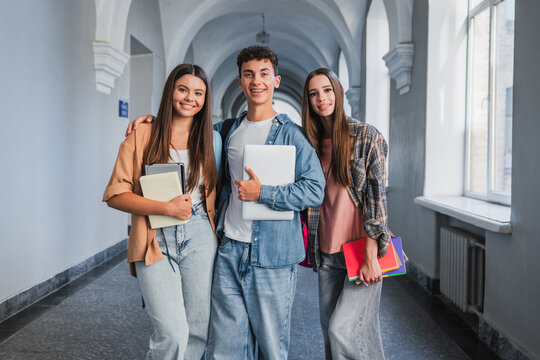 Group of teenage students looking at camera in hallway, confident classmates with textbooks, modern education, school community, learning and academic success concept