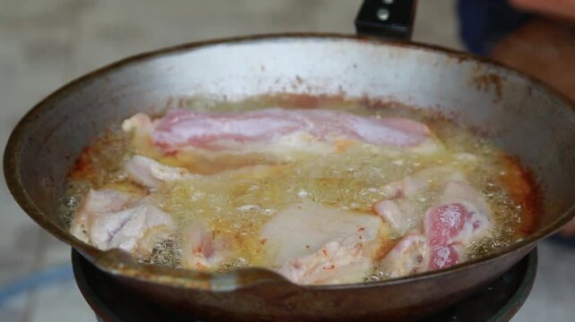 Pork frying in hot bubbling oil inside a cast iron pan on a gas stove. Cooking traditional Thai food, street food preparation, and delicious crispy meat concept.