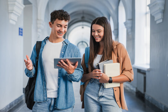 Male and female students standing in school corridor looking at tablet screen, digital learning, education technology, teamwork and modern study concept
