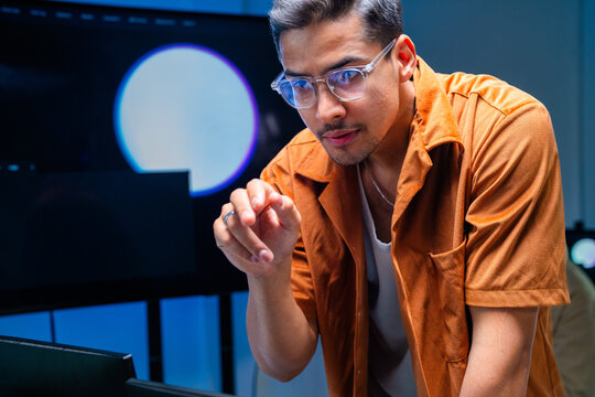 A focused dark-haired cybersecurity analyst sits at the keyboard facing the camera inside a dark security operations centre at night, tracking suspicious activity across enterprise systems.