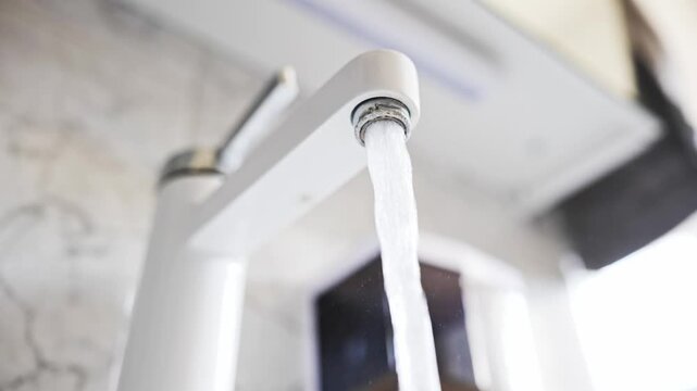 Strong stream of water flowing from the calcified aerator of a modern white bathroom faucet in a low angle shot in slow motion