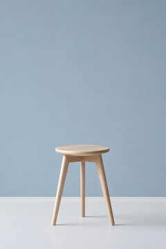 Light wooden three legged stool against soft blue wall minimal interior
