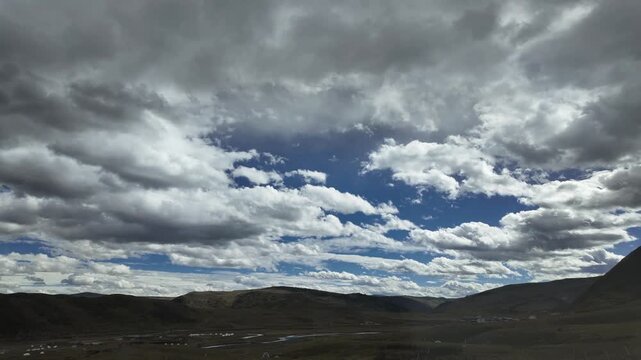The stunning natural scenery displays a wide expanse of valley under a blue sky decorated with thick and dramatic formations of white and gray cumulus clouds.
