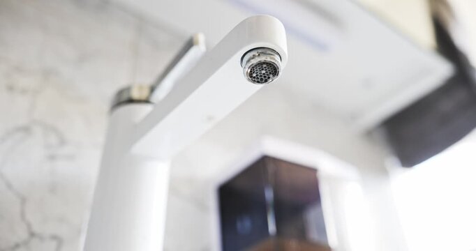 Water dripping slowly from the calcified aerator of a modern white bathroom faucet in a low angle shot in real time.