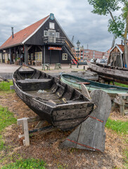 Weathered wooden rowing boats and large rudder blades are displayed beside a traditional black timber clubhouse with a red tiled roof. The maritime heritage scene represents historic boatbuilding, row © Volha