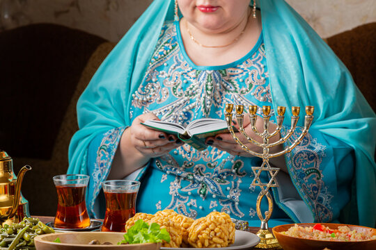 A Jewish woman prays from the siddur at a table with lit Shabbat candles