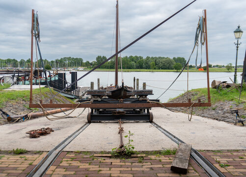 Heavy steel boat cradle stands on rails leading down a concrete slipway toward the harbor. Ropes, chains, lifting frames and wooden boats illustrate traditional vessel launching, haul-out maintenance,