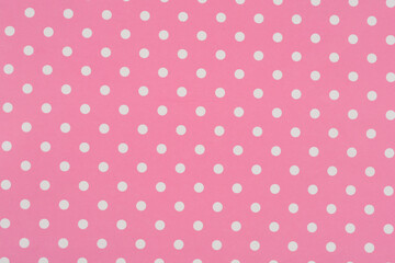 A full frame background texture shows a seamless and sweet pattern of small white polka dots evenly distributed across a pink paper surface. © nahhan