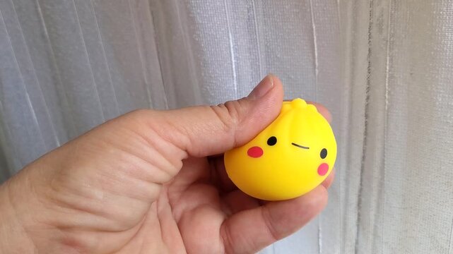 Cute, soft, yellow sensory toy in a person's hand. Rolling a squishy anti-stress dumpling with your fingers relieves stress and tension. Moldova, Chisinau, July 5, 2026