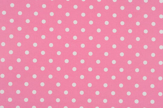 A full frame background texture shows a seamless and sweet pattern of small white polka dots evenly distributed across a pink paper surface.