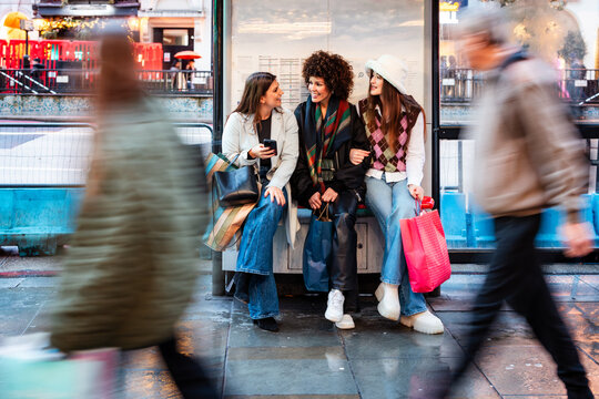 Women friends talking at London bus stop after shopping