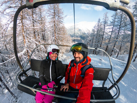 Couple enjoying winter vacation riding ski lift up mountain