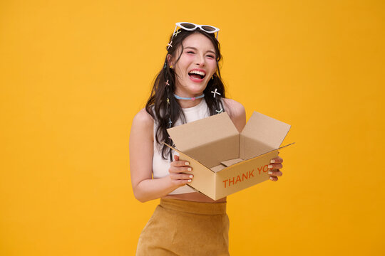Asian woman holding an open delivery box and laughing expressing ecommerce satisfaction unboxing excitement customer appreciation online retail convenience and joyful purchase experience.