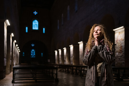 Spiritual woman praying with hands clasped in faith inside a dark historic church with soft light on her face