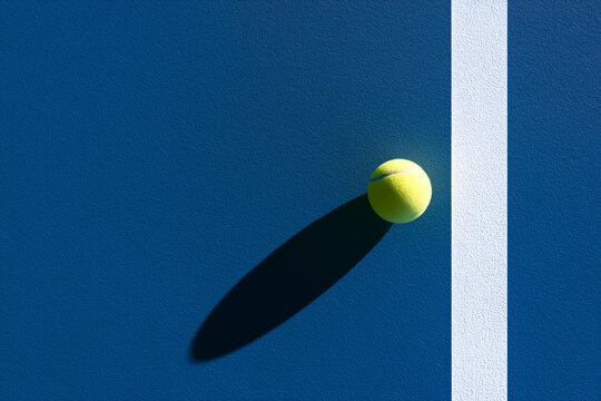 Minimalist photorealistic composition of a tennis ball casting a long dramatic shadow across a blue tennis court, with clean geometry, premium commercial lighting and generous copy space