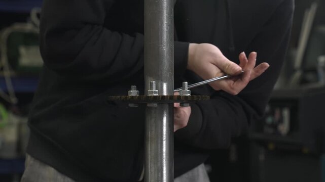 A worker tightens nuts on bolts with a wrench while installing a sprocket for a transmission mechanism onto which a chain will later be placed