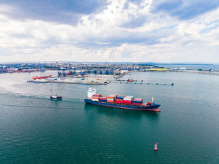 Large cargo ship sails through the waters near a busy port while a tugboat assists during daylight hours © DSMT