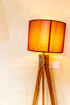 Warm Wooden Tripod Floor Lamp With Orange Lampshade Against Stone Wall For Cozy Interior