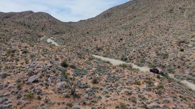 Aerial view shows an SUV pulling a teardrop camper trailer across dirt trails in Anza Borego Desert, moving through hills and mountains.